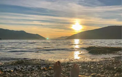 a person laying on a beach with their feet in the water at 3 Bedroom Beautiful Home In Vik I Sogn in Stadheim