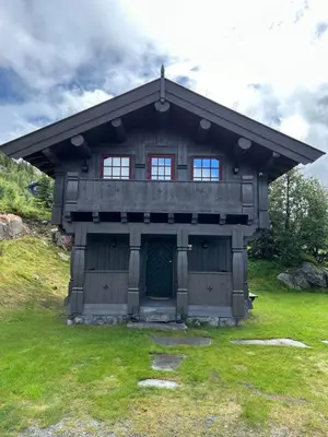 a wooden house with a green door in a field at Eventyrtunet in idyllic Tuddal in Hjartdal