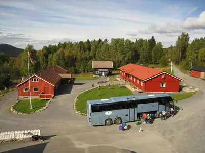 a bus parked in a parking lot in front of red buildings at Camp Sjusjøen in Mesnali