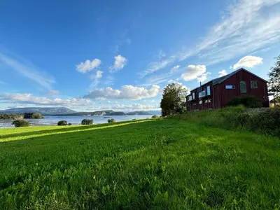 a red barn on a grassy hill next to a lake at Stenegården in Namsos