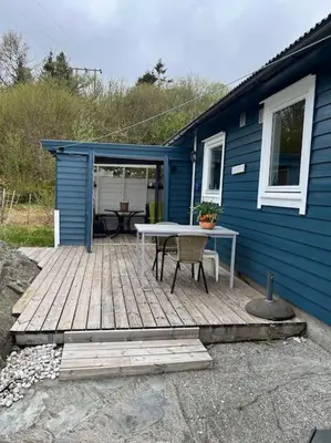 a blue house with a wooden deck with a table at Holiday Home Sletta in Sletta