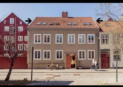 a woman walking in front of a large house at Nydelig leilighet i Bakklandet in Trondheim