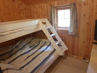 a bunk bed in a wooden room with a window at Idyllic lakeside cabin with private beach and boat in Vassli