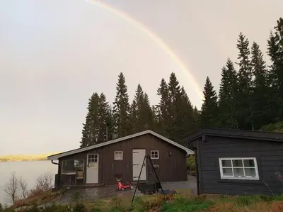a rainbow is in the sky over a house at Idyllic lakeside cabin with private beach and boat in Vassli