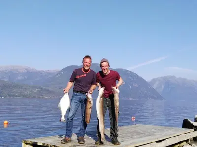two people standing on a dock with two fish at Fjordhytte-2 am Hardangerfjord, grandioses Fjordpanorama, 20 PS Motorboot mietbar! in Ænes