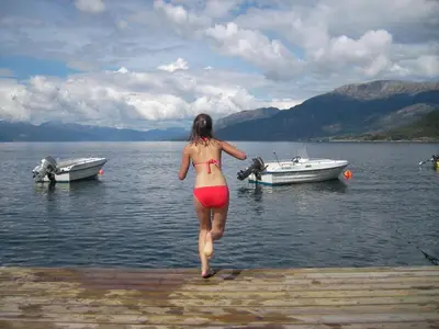 a woman in a bikini walking into the water with boats at Fjordhytte-3 in traumhafter Lage 100 Meter vom Hardangerfjord, Motorboot mietbar in Ænes