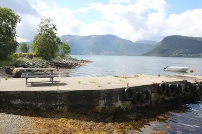 a bench on the shore of a lake with a boat at Fjordhytte-38 bei Rosendal am Hardangerfjord in Rosendal