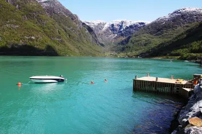 a boat in a lake with people in the water at Fjordhytte-6 direkt am Maurangerfjord, einem Seitenarm des Hardangerfjords in Sundal