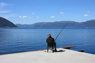 a person sitting on a dock fishing on a lake at Fjordhytte-23 direkt am Sognefjord, mit mietbaren Motorbooten 9,9-60 PS in Bjordal