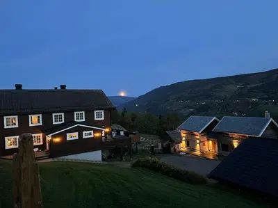 a large house with lights on in the yard at Rudland Gård - Unik gårdsovernatting i stabbur fra 1750 in Sør-Fron
