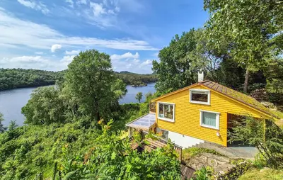 a yellow house on a hill next to a river at 1 Bedroom Stunning Home In Haugesund in Haugesund