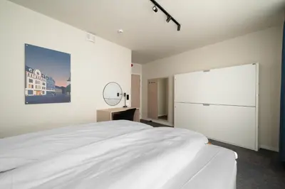 a white bedroom with a large bed and a mirror at BREEZE Hotel Victoria - Self-Service in Bergen