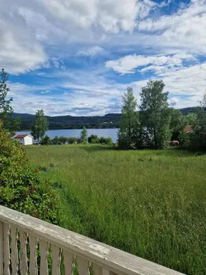 a field with a fence and a view of a lake at Åsenfjord, feriehus ved sjøen in Hopla