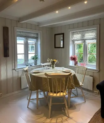 a dining room with a table and chairs and windows at Veslegarden in Lærdalsøyri