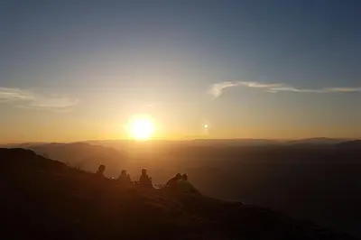 a group of people sitting on a hill watching the sunset at Feriehus i Lærdal in Mjeldo