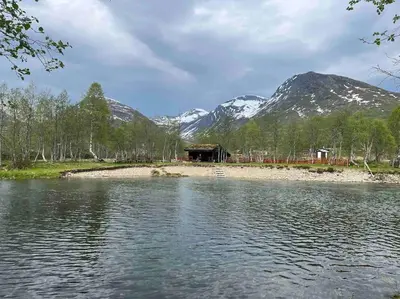 a cabin on the shore of a lake with snow covered mountains at Leilighet Overøye Hyttegrend in Stordal