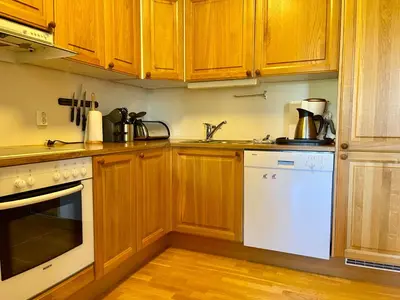 a kitchen with wooden cabinets and a white dishwasher at Spacious Apartment In Central Beitostølen in Beitostøl