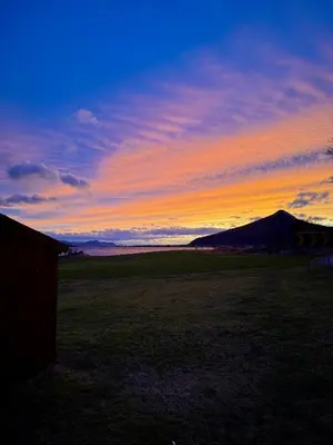 a sunset in a field with a mountain in the background at Sjønært feriehus, båt tilgjengelig for leie in Ålesund