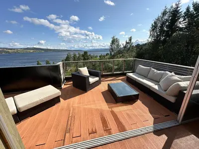 a deck with couches and tables and a view of the water at Moderne og familievennlig bolig, nær populær strand ved Mjøsa in Gjøvik