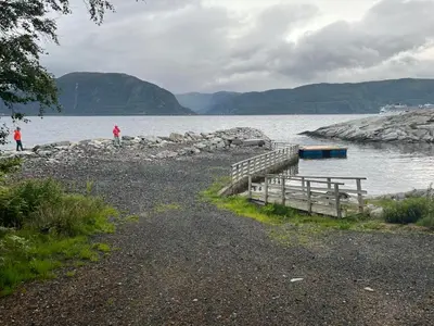 a dock on a body of water with people walking on the shore at Alværa Misionssenter Sommerhotel in Lavik