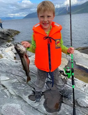a young boy wearing a life vest holding a fish at Alværa Misionssenter Sommerhotel in Lavik