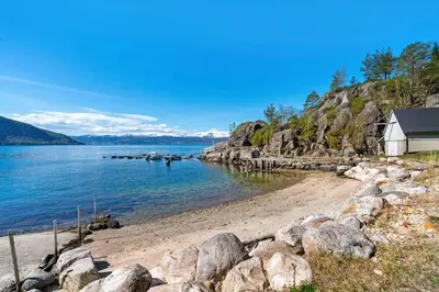 a beach with rocks and a house and the water at Cozy cabin, minimum 5 nights in Oppheim