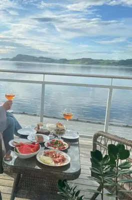 a table with plates of food and drinks on a balcony at seaside house with stunning sunsets & sun all day Near Trondheim in Buvika