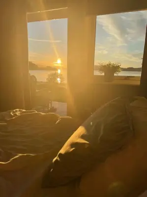 a bedroom with a bed and a window with the sunset at seaside house with stunning sunsets & sun all day Near Trondheim in Buvika