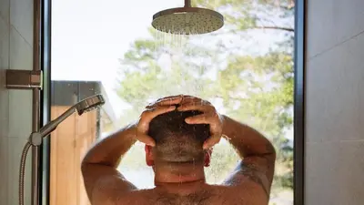 a man standing in a shower under a shower head at Speilsuite med egen badstue og panorama in Steinkjer