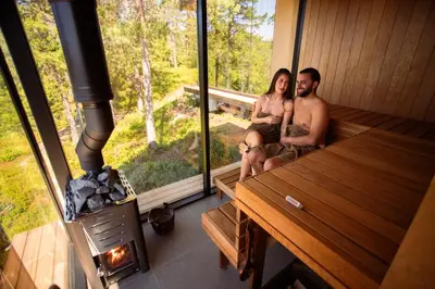 a man and woman sitting in a sauna with a wood stove at Speilsuite med egen badstue og panorama in Steinkjer
