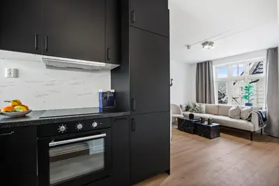 a kitchen with black cabinets and a living room at Homerentals Apartments - Behind Bryggen & historic cobblestone streets - 2 Floor renovated from february 2025 in Bergen