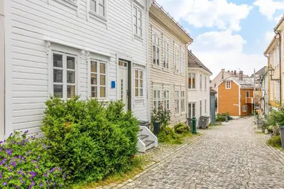 a cobblestone street with white houses and flowers at Homerentals Apartments - Behind Bryggen & historic cobblestone streets - 2 Floor renovated from february 2025 in Bergen