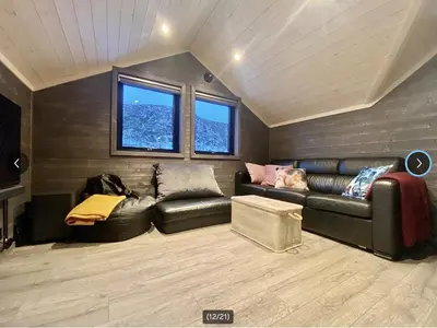 a living room with a leather couch and two windows at Fjellhytte med ski inn-ut in Torvetjørn
