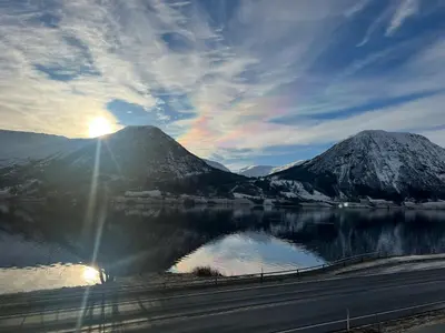 a view of a mountain and a lake with the sun at Husslåttene apartments in Skei