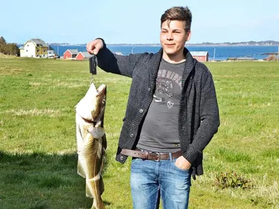 a man is holding a fish in a field at 11 person holiday home in Fjørtoft-By Traum in Fjørtoft