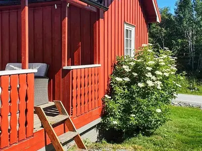 a red house with a bench next to a bush at 6 person holiday home in Storfosna-By Traum in Sletta