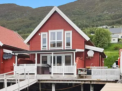 a red house with a deck and mountains in the background at 6 person holiday home in Gursken-By Traum in Larsnes