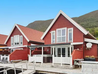 a red house with a wooden deck and mountains in the background at 6 person holiday home in Gursken-By Traum in Larsnes