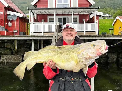 a man holding a large fish in front of a house at 6 person holiday home in Gursken-By Traum in Larsnes