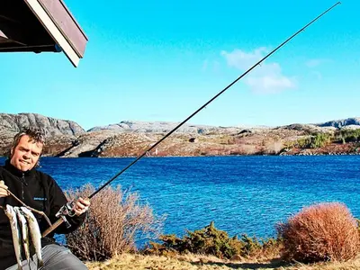 a man holding a fishing pole next to a body of water at 12 person holiday home in Kvenvær in Kvenvær