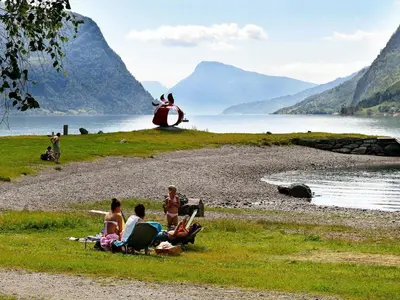 a group of people sitting on the grass near a lake at 6 person holiday home in Øvre Årdal in Øvre Årdal