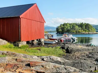 a red building with boats in a body of water at 5 person holiday home in VÅGLAND in Bårdset