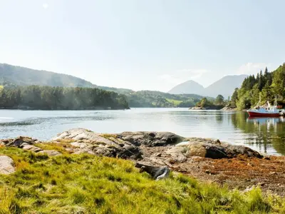 a boat on a river with mountains in the background at 5 person holiday home in VÅGLAND in Bårdset