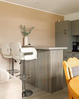 a kitchen with a bar with white bar stools at Vestre apartment in Ålesund