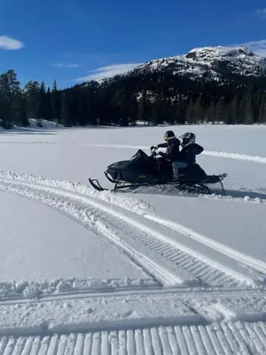 two people riding on a snowmobile in the snow at Hytta på Øyfjell in Trovatn