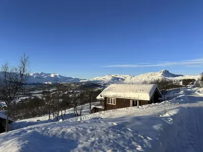 a cabin covered in snow with mountains in the background at Perfect Couple's Hideaway In Nature! in Beitostøl