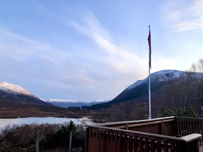 a flag pole on a deck with a lake and mountains at Peaceful cabin retreat in the Norwegian mountains in Ulsteinvik