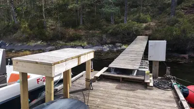 a wooden dock next to a boat in the water at Gunnarhytta, Valevåg in Valevåg