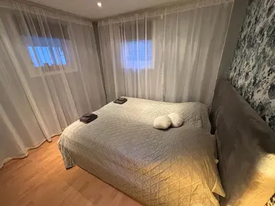 a bedroom with a bed with white sheets and two windows at Cozy Apartment in Ålesund