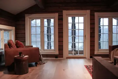 a living room with three windows and a couch at Tømmerhus i Geiranger Sentrum med panorama utsikt in Geiranger